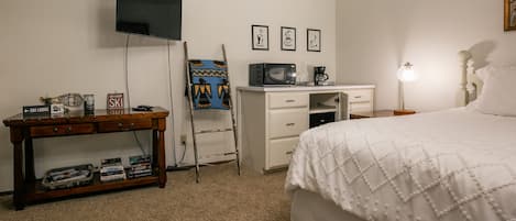 Un dormitorio con cama, escritorio, televisor, cafetera y lámpara.