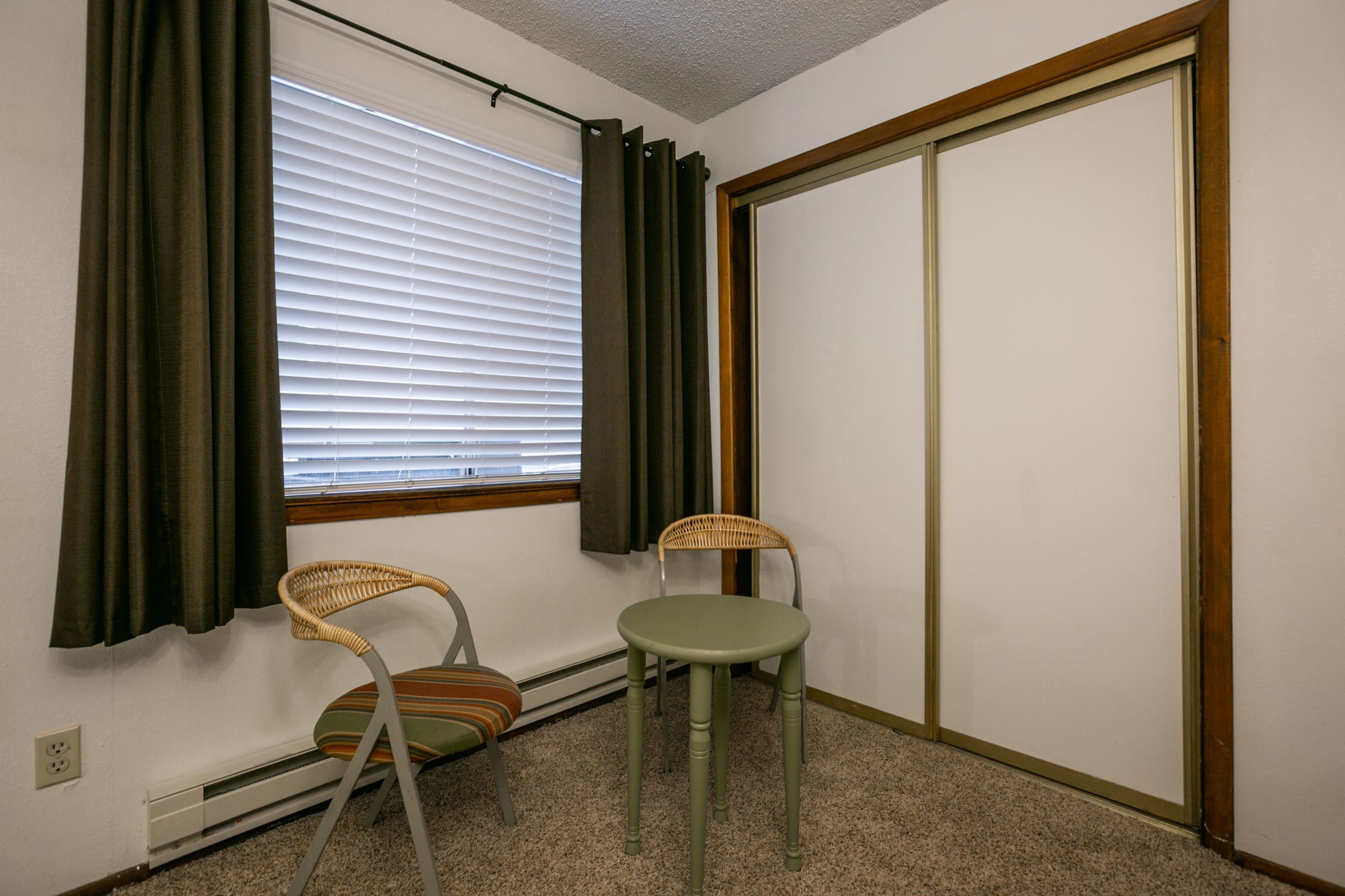 Ein Zimmer mit Fenster, zwei Stühlen, einer Heizung und einer Tür.