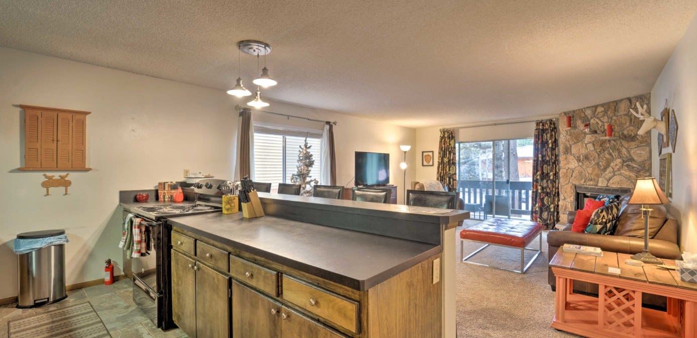 Cozinha com ilha central, sala de jantar com sofá e mesa, e sala de estar com lareira.