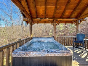 Un jacuzzi bajo una cubierta de madera con baranda, rodeado de árboles.
