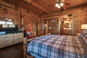 Un dormitorio tipo cabaña de troncos con colcha escocesa, un televisor sobre un aparador, un árbol de Navidad y un letrero que dice "Top of the Dog".