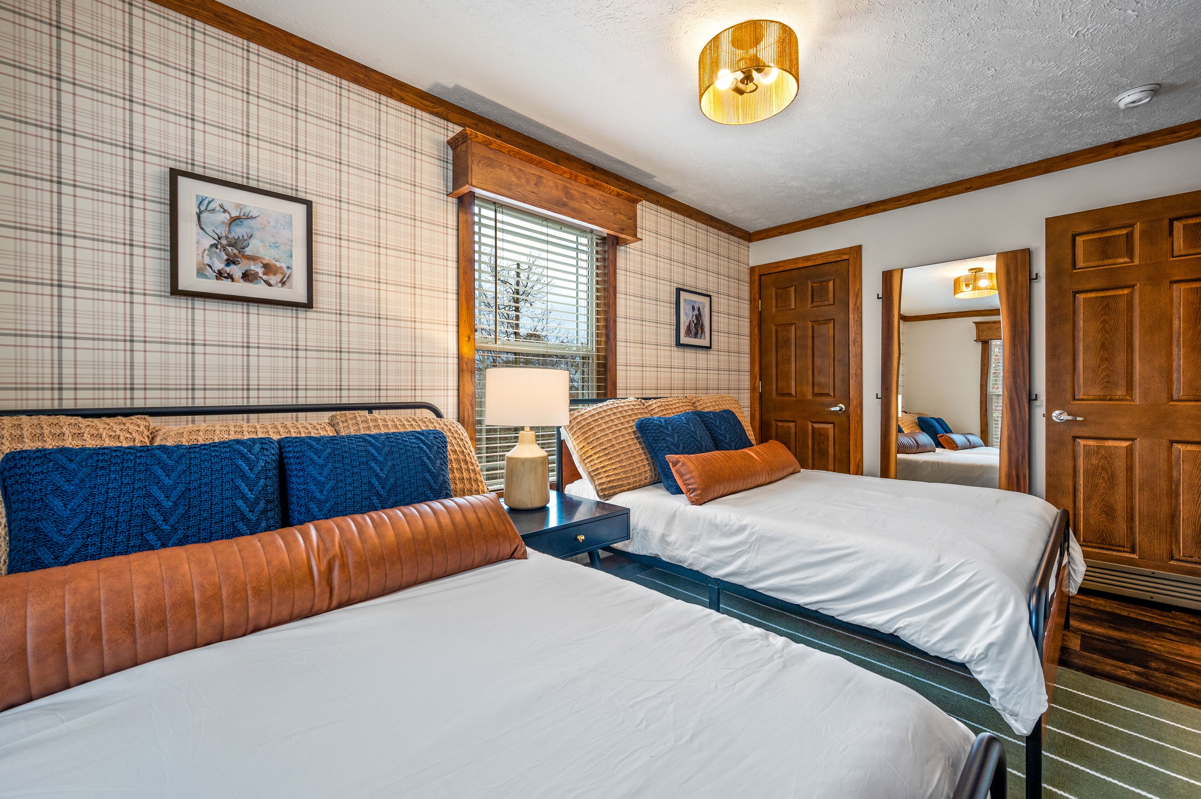 A hotel room with two beds, a window with blinds, a lamp, and a wooden door.