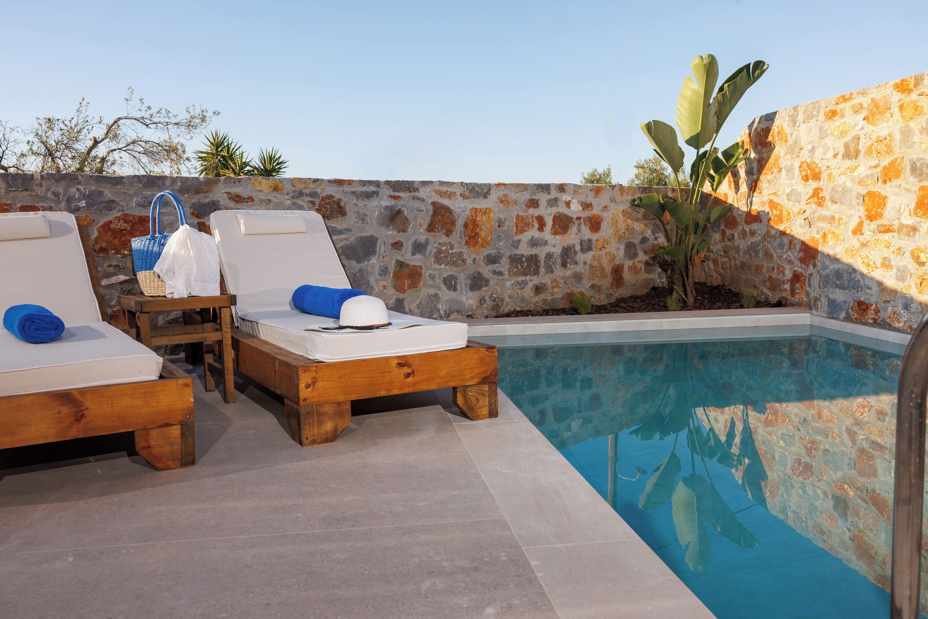 A poolside area with wooden lounge chairs and a stone wall.