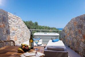 Une terrasse aux murs de pierre, avec une table en bois, un jacuzzi et une vue sur la mer.