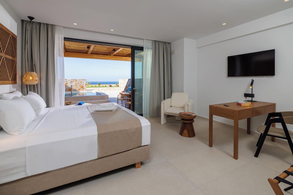 A hotel room with a bed, a TV, a desk, and a view of the ocean.