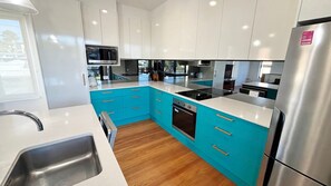 A modern kitchen with white cabinets, a blue countertop, stainless steel appliances, and a wooden floor.
