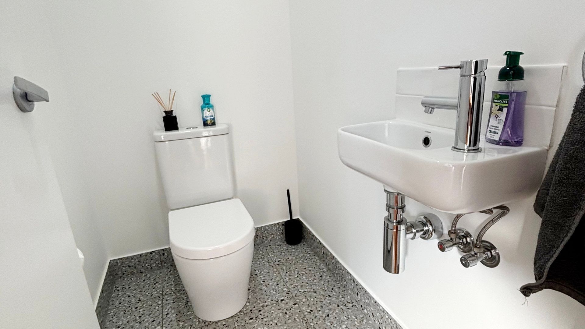 Un baño pequeño con inodoro blanco, lavamanos y escobilla.