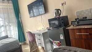 A compact hotel room with a bed, a desk with a chair, a kitchenette with a stove and microwave, and a TV mounted on the wall. - Jiji poa (Nairobi)