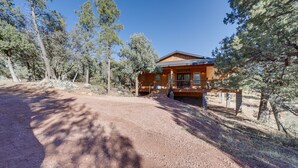 Une cabane en bois dotée d’un porche couvert, entourée de pins et bordée d’un sentier de terre.