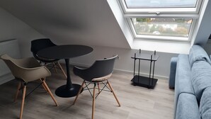 Ein modernes Schlafzimmer im Loft-Stil mit Dachfenster, einem runden Esstisch, zwei Stühlen, einer Couch und einer schwarzen Stehlampe.