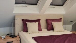 Ein Schlafzimmer mit einem Bett, zwei Oberlichtern, einem Nachttisch und einem Beistelltisch.