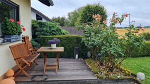 Eine Holzterrasse mit Tisch und Stühlen, umgeben von einem Garten mit verschiedenen Pflanzen und Blumen.