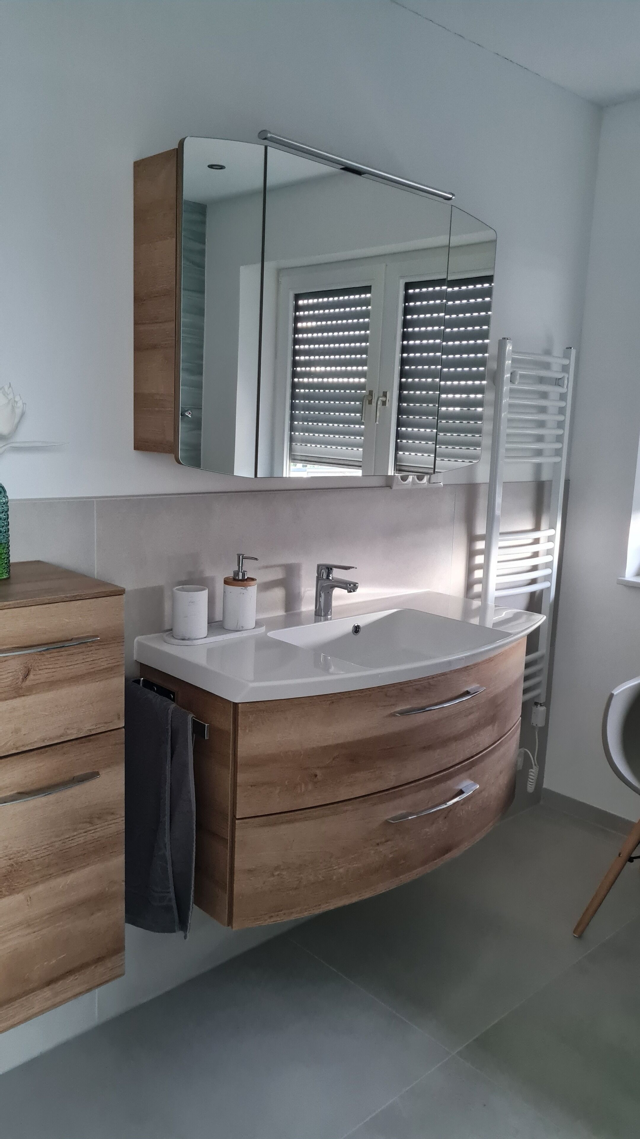 A modern bathroom with a wooden vanity, a large mirror, and a built-in heater.