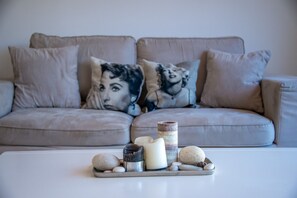 Een beige bank met gekleurde kussens, een witte salontafel met kaarsen, stenen en een pot.