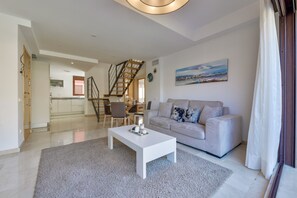 A modern living room with a white sofa, a coffee table, and a staircase leading to an upper floor.