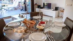A dining area with a glass table, chairs, plates, cutlery, and a basket of bread.