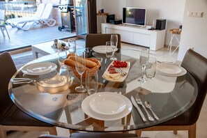 A dining area with a glass table, chairs, plates, cutlery, and a basket of bread.