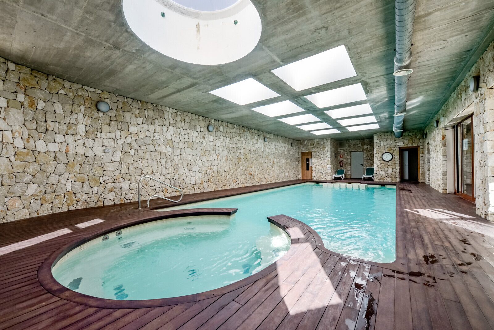 An indoor swimming pool with stone walls, a wooden deck, and skylights.