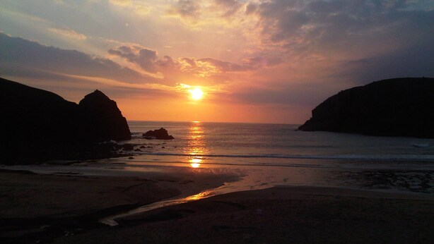 A sunset over a beach with rocky formations on either side. - 27 Garenin (Isle of Lewis)