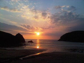 A sunset over a beach with rocky formations on either side. - 27 Garenin (Isle of Lewis)
