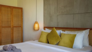 A hotel room with a bed, pillows, a hanging light fixture, and a wooden wardrobe. - Joy Villa by Betterplace (Canggu)