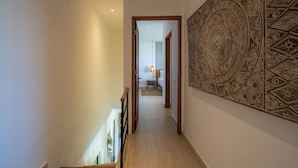 A hallway with a patterned wall, a staircase, and a door leading to a room with a bed and a lamp. - Joy Villa by Betterplace (Canggu)