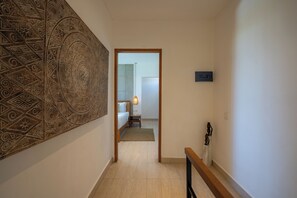 Un pasillo con papel tapiz decorativo, una cama, una mesita de noche, una lámpara colgante y una puerta que da a un baño.