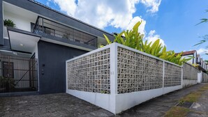 A modern building with a balcony, a gated entrance, and a white fence with greenery. - Joy Villa by Betterplace (Canggu)