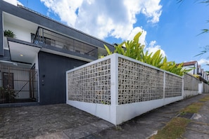 A modern building with a balcony, a gated entrance, and a white fence with greenery. - Joy Villa by Betterplace (Canggu)