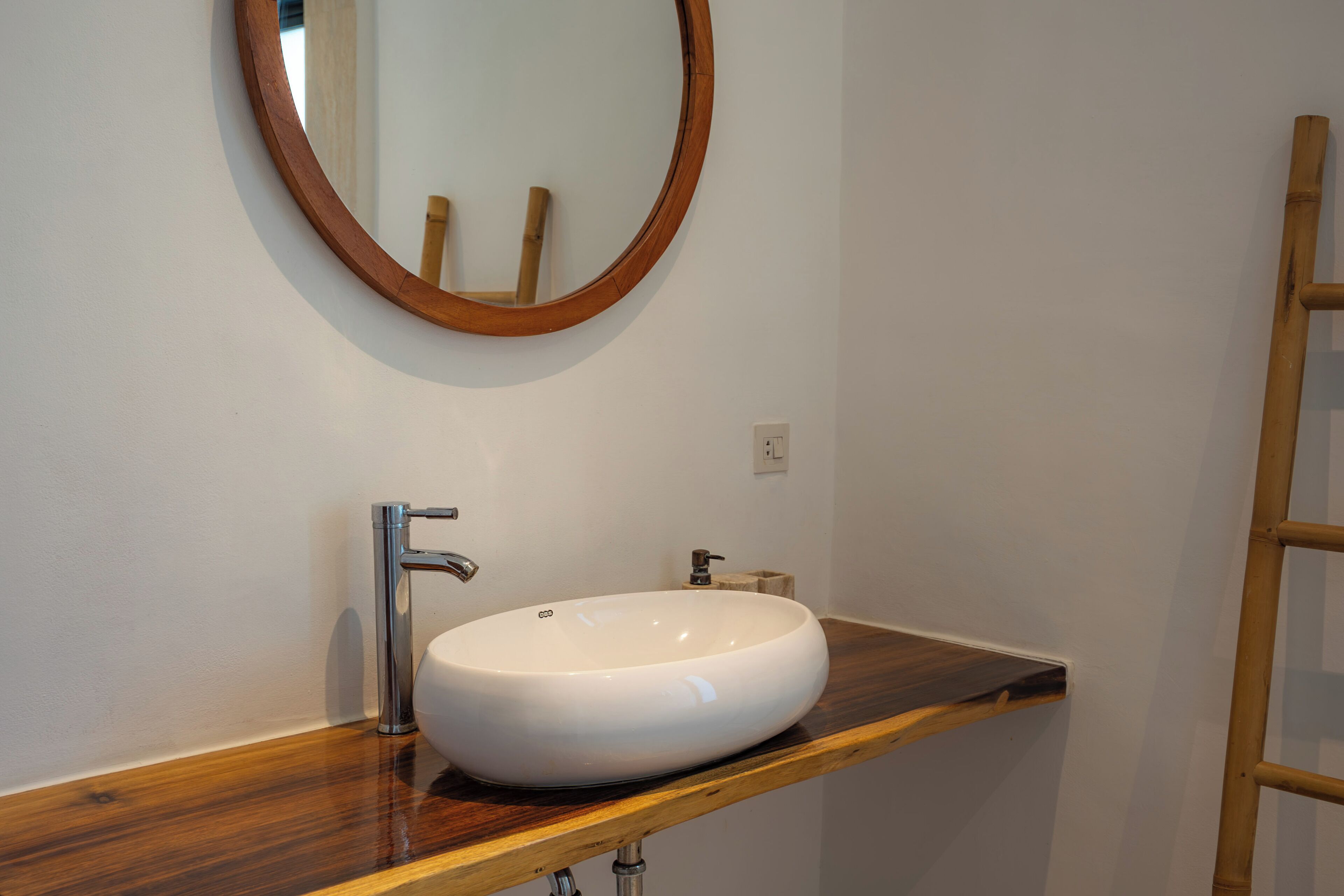 A bathroom with a wooden vanity, a white sink, and a round mirror.