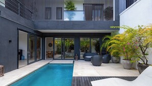 A modern outdoor pool area with a wooden deck, lounge chairs, and potted plants. - Joy Villa by Betterplace (Canggu)