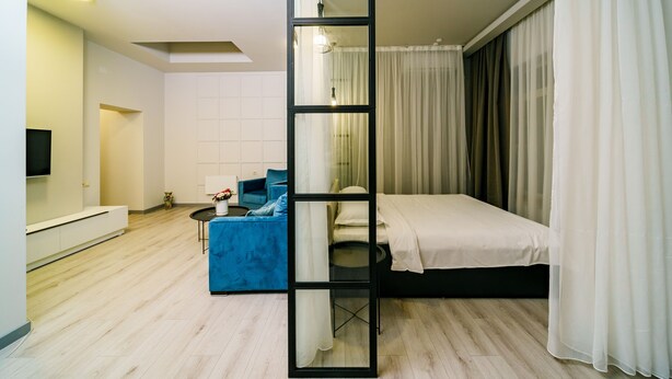 A modern bedroom with a bed, a blue sofa, a large mirror, and a TV on the wall.