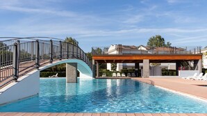 A swimming pool with a wooden deck, a curved metal railing, and lounge chairs. - Lovely Apartment Overlooking the Pool in Bibione (San Michele al Tagliamento)