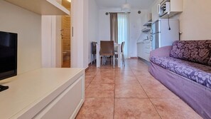 Un espacio habitable compacto con televisor, sofá, mesa de comedor y kitchenette.