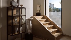 Un interior moderno con una escalera que lleva a un balcón, una vitrina de cristal con objetos decorativos y vistas al exterior.