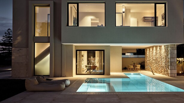 Una casa moderna de dos pisos con piscina, ventanas amplias y un muro de piedra.