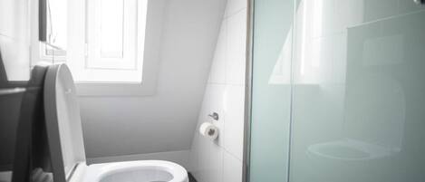A modern bathroom with a toilet, a glass shower enclosure, and a window providing natural light.