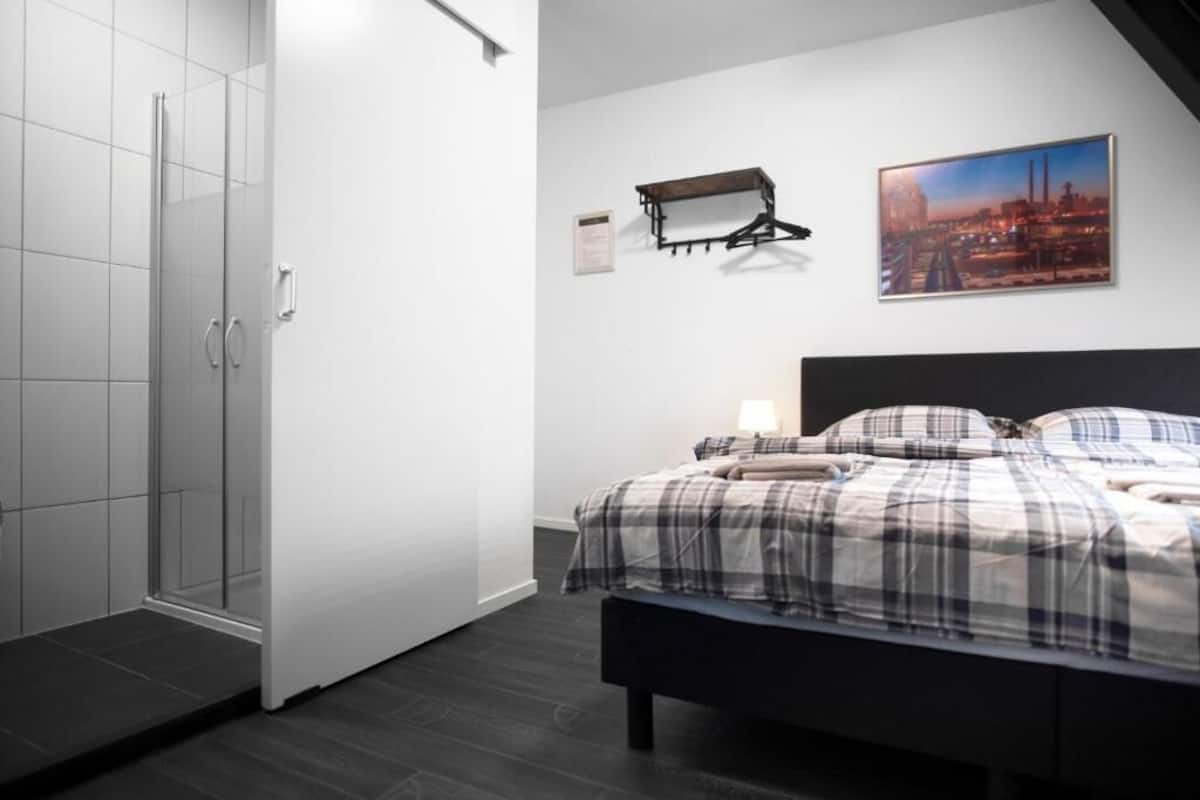 Quarto com cama, um banquinho, porta-roupas e uma pintura da paisagem urbana.