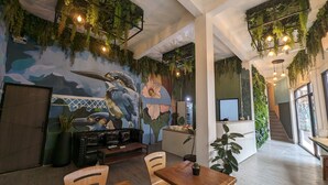 Un restaurante con un mural de un pájaro, muebles de madera y plantas colgantes.