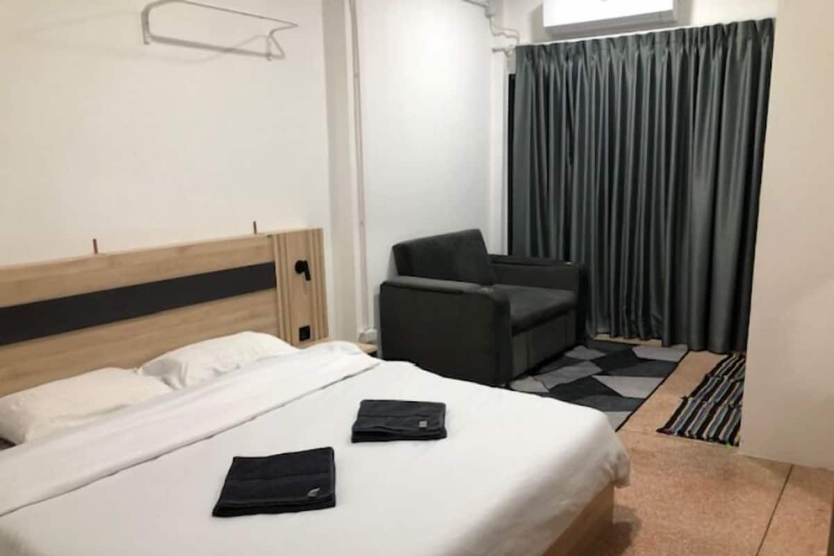 Une chambre d’hôtel avec un lit, une chaise, un bureau et une fenêtre avec des rideaux.