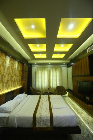 A hotel room with a large bed, a TV, a seating area, and a decorative wall.