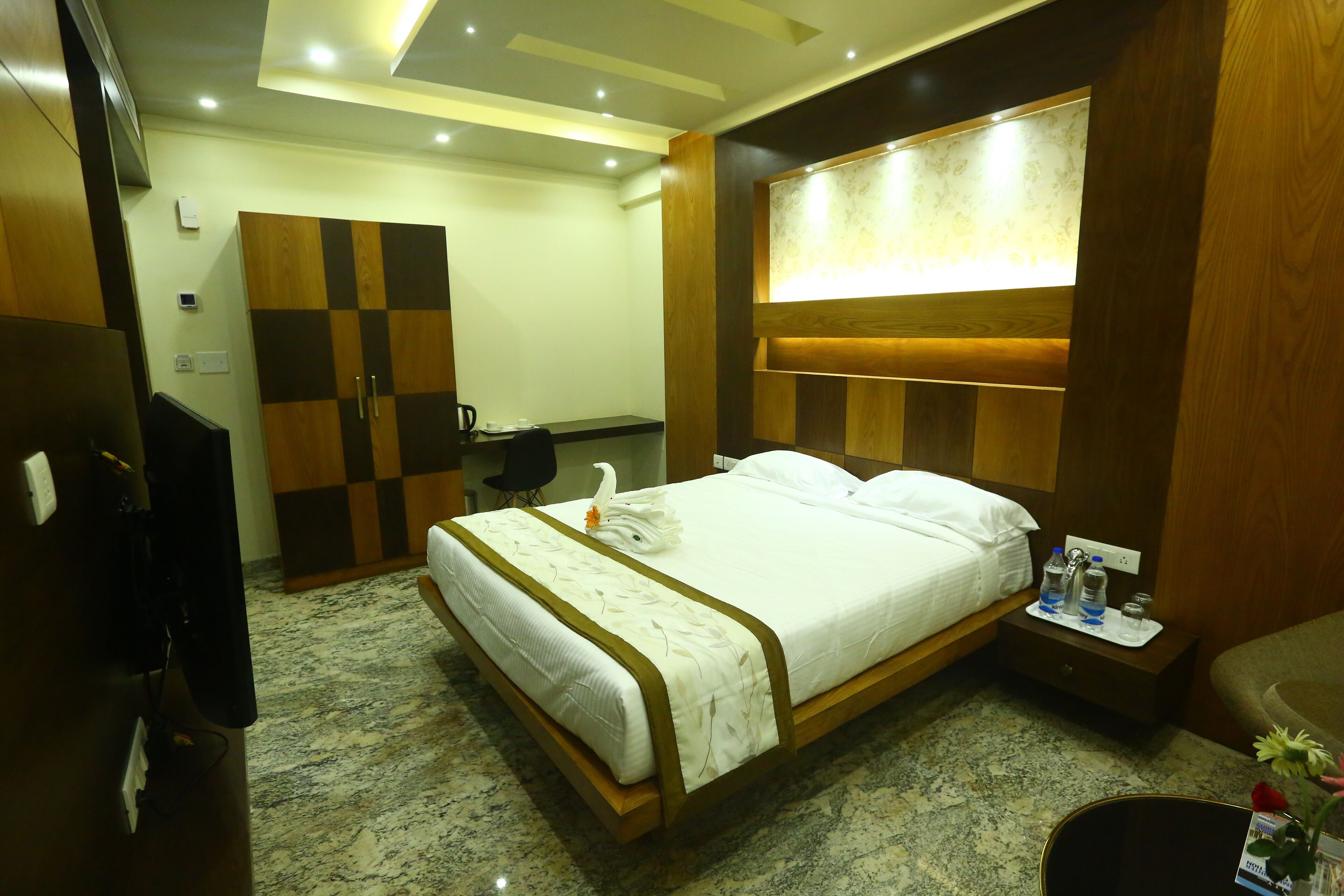A hotel room with a bed, a desk, a wardrobe, and a nightstand with toiletries.