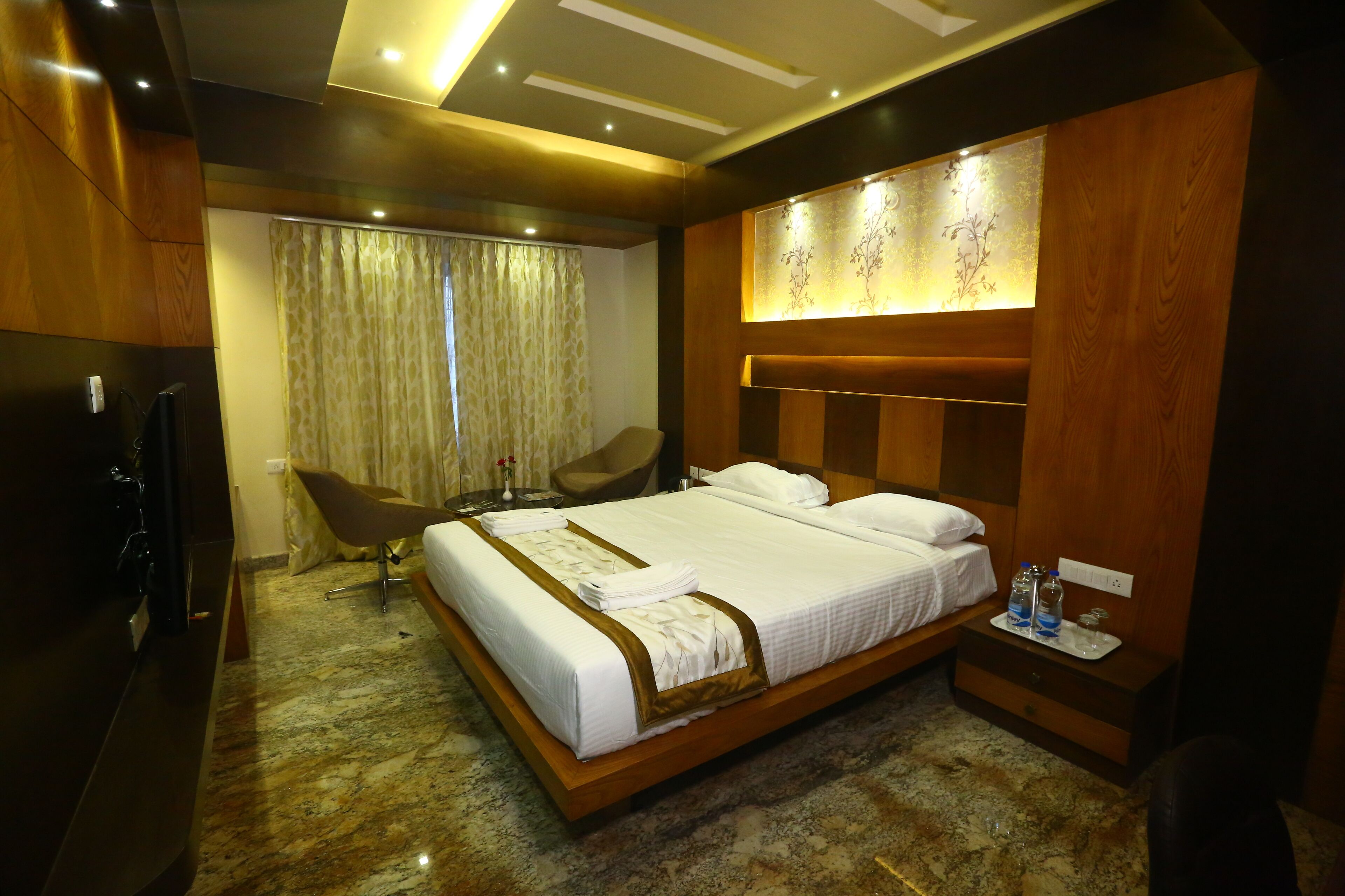 Quarto de hotel com uma cama grande, cabeceira de madeira, televisão de tela plana, escrivaninha com cadeira e janela com cortinas.