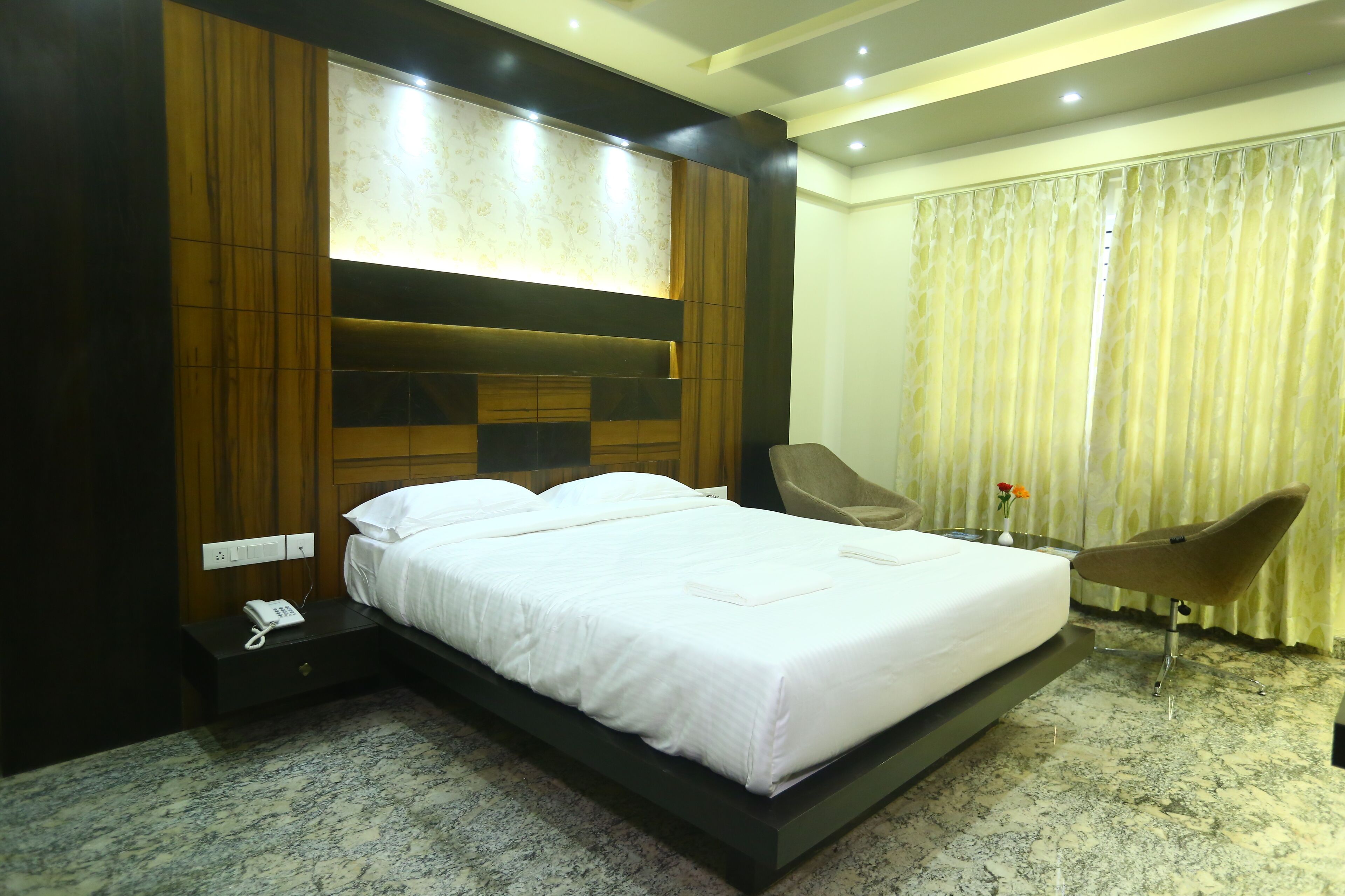 A modern hotel room with a large bed, a bedside telephone, a chair, and a curtain.