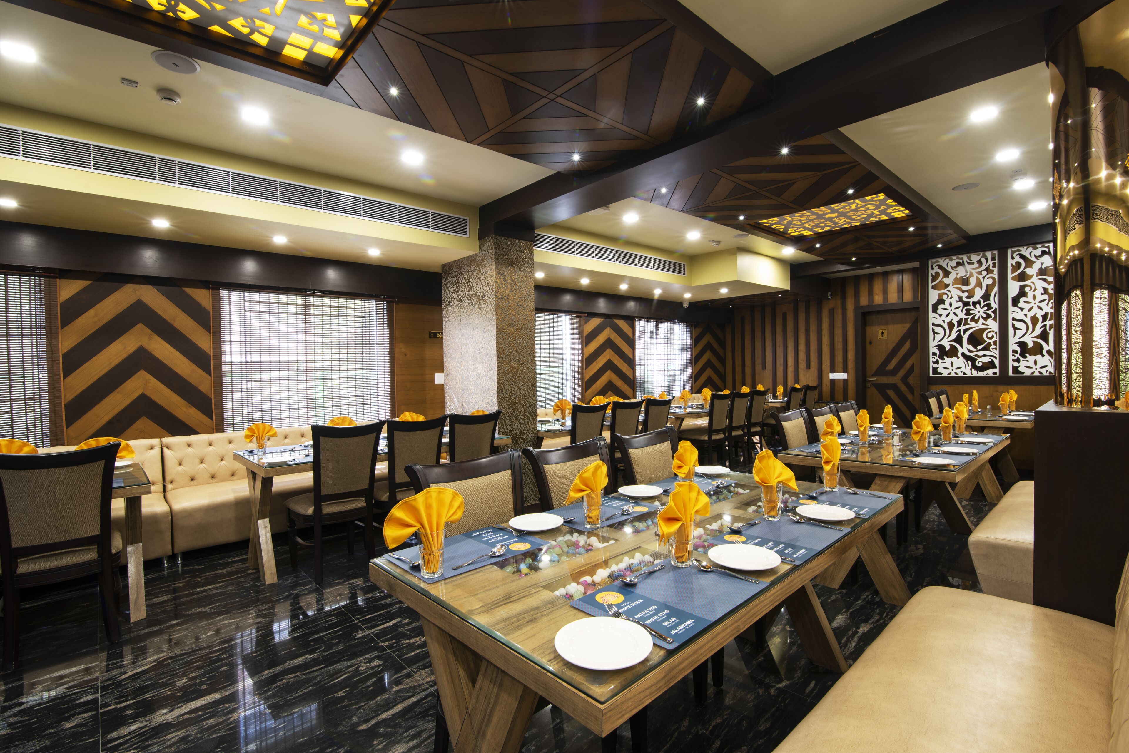 A dining area with multiple tables set for service, featuring a modern design with geometric wall patterns and a high ceiling.