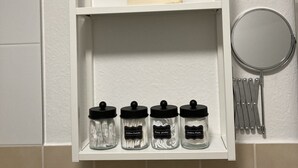 Une étagère de salle de bain avec un miroir, une petite plante et trois pots étiquetés avec des produits de toilette.