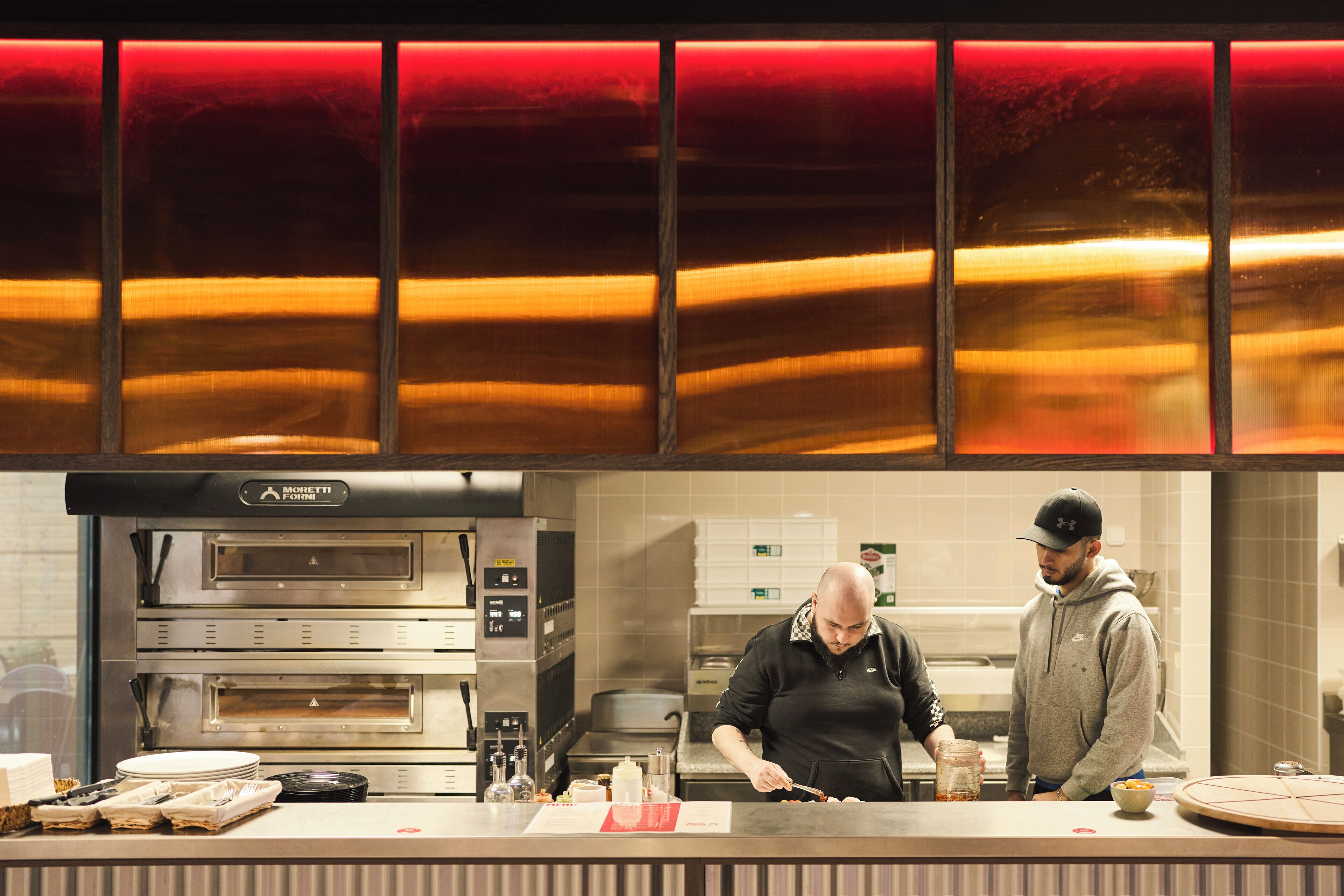 Une cuisine professionnelle équipée de deux fours, d’un comptoir où sont disposés des aliments, et d’une personne qui prépare des plats.