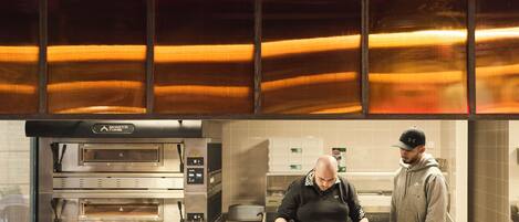 A commercial kitchen with two ovens, a counter with food items, and a person preparing food.