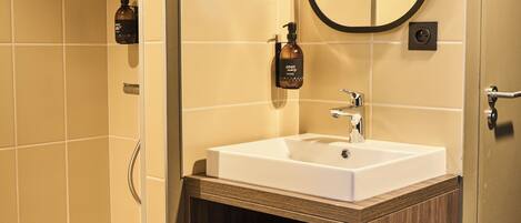 A modern bathroom with a walk-in shower, a wooden vanity with a white sink, and a mirror with a black frame.