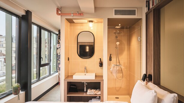 A modern hotel room with a large bed, a bathroom with a shower, a sink, and a mirror.
